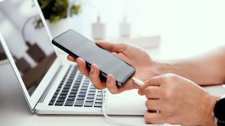 Person plugging a smartphone into a laptop to charge.