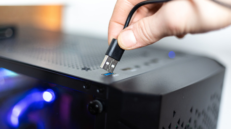Person plugging USB cable into port on desktop PC.
