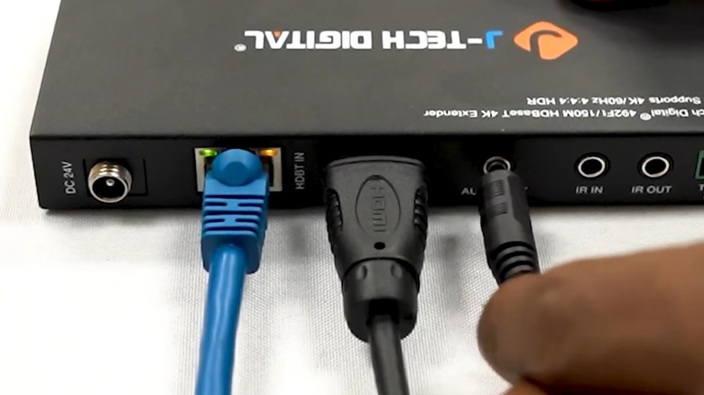 HDMI extender placed on a white surface with an HDMI cable and ethernet cable plugged into it