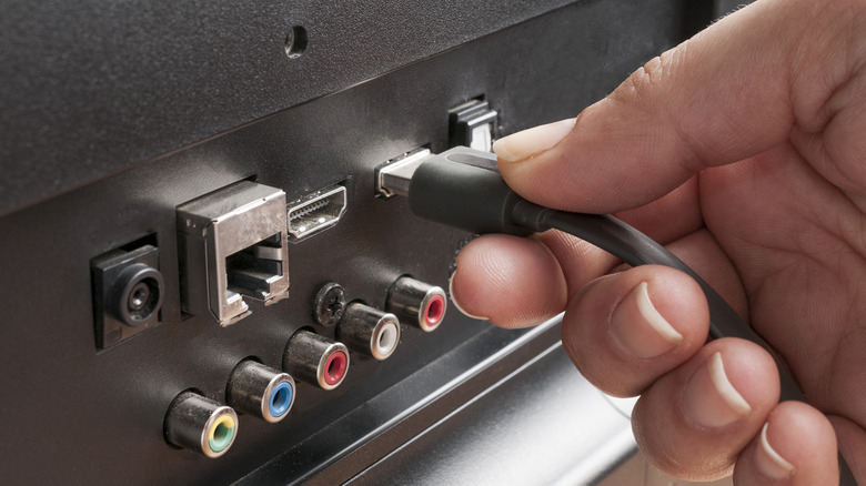 Person plugging an HDMI cable into the back panel of a TV