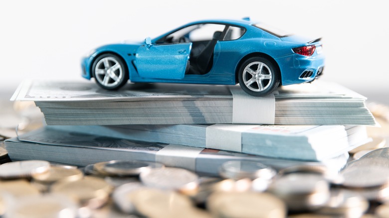 A blue toy car with its side door open placed on top of a pile of banknotes and coins.