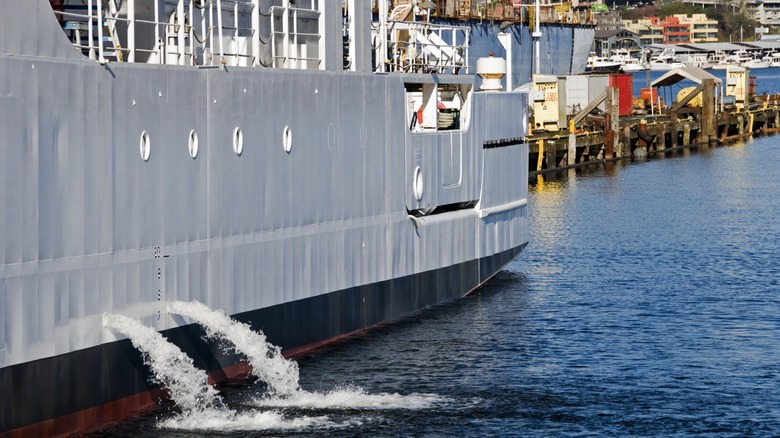 Barco acoplado gris en un puerto, derramando agua de sus tanques de lastre
