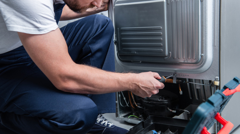 Partial view of a repairman fixing a refrigerator