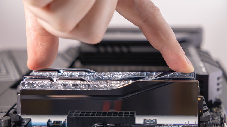 Hand pressing RAM stick down into motherboard