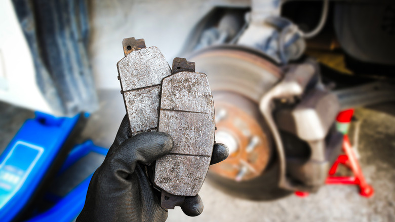 A technician holding worn brake pads, with the brake disc and calipers in the background