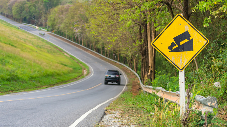 A steep slope sign next to a winding road with cars