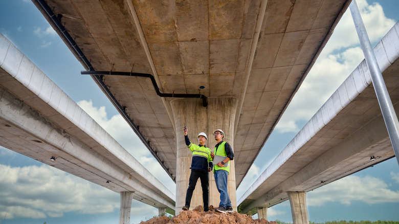 Civil engineers inspect highway construction site with concrete road structures overhead