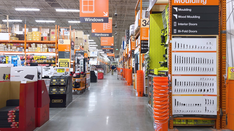 A bright, orderly aisle of a home improvement store, with a forklift actively restocking supplies.