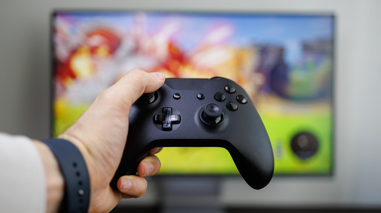 A hand holding a game controller in front of a monitor