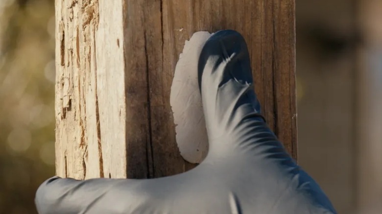 A person applying J-B Weld putty to wood.