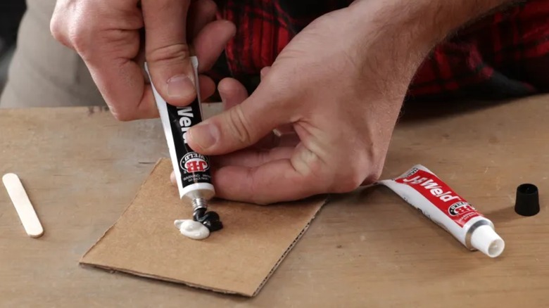 A person mixing J-B Weld on cardboard.