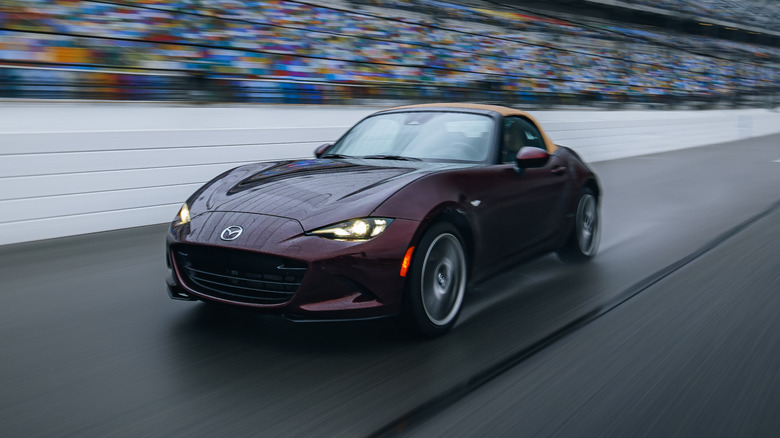 A dark purple Mazda MX-5 35th Anniversary Edition on a wet race track, front 3/4 view