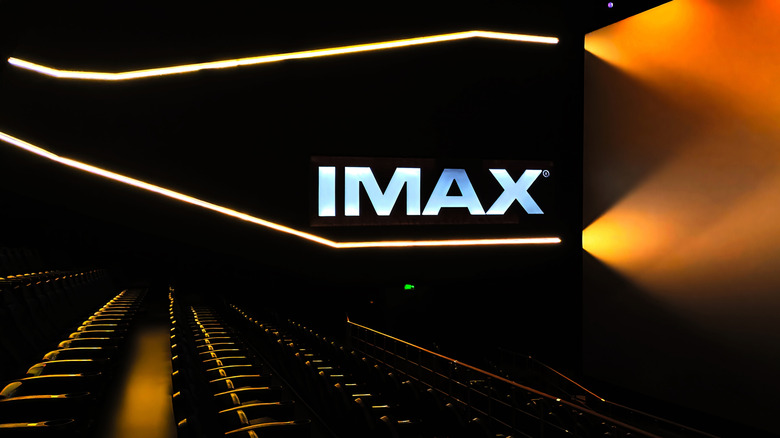 Inside of a dark IMAX theater with an illuminated IMAX logo on the wall