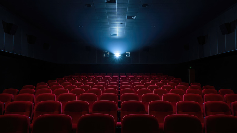 An empty movie theater of red seats with the light from a projector shining from the back of the theater