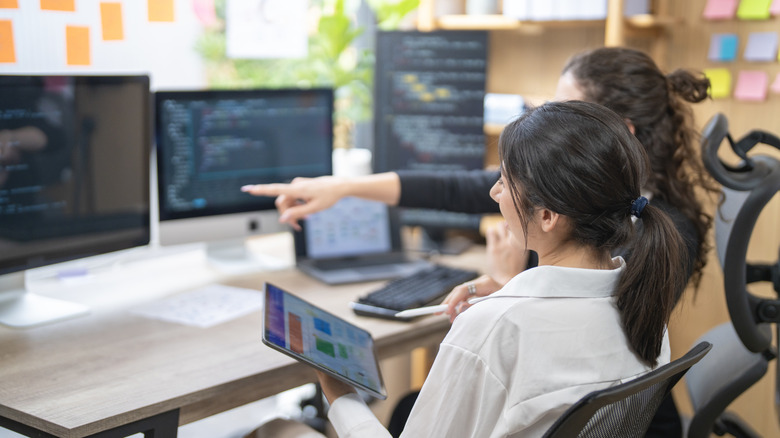 Dos profesionales colaboran en un entorno de oficina moderno utilizando varias pantallas de computadora.