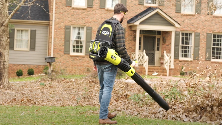 Man blowing leaves with Ryobi blower in front of house