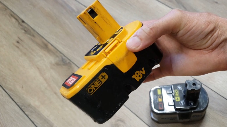 Hand holding a nickel-cadmium Ryobi battery over a wooden table.