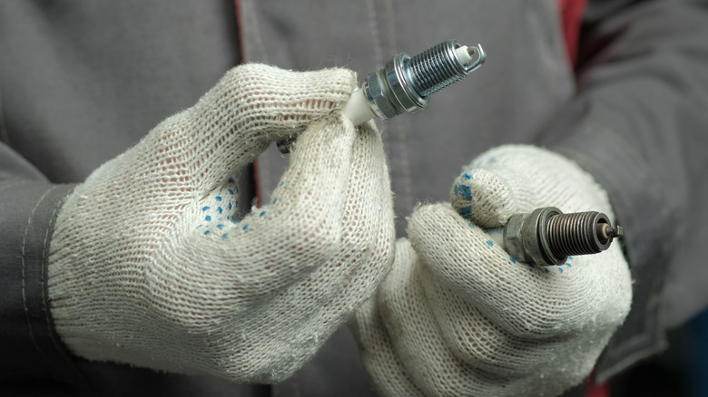 Service technician holding a new and old spark plug in each hand