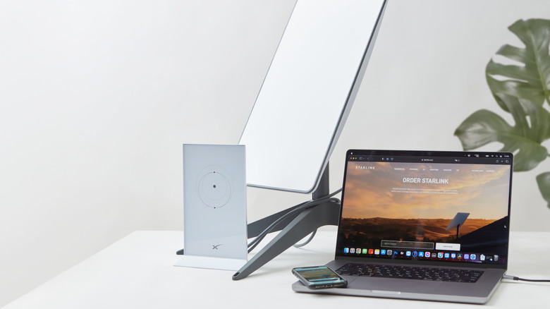 Starlink dish and router on a table with a laptop and phone