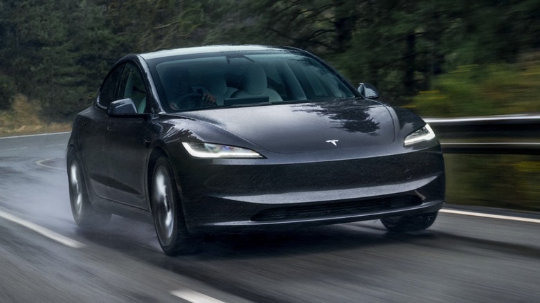 Black Tesla Model 3 driving down forested road