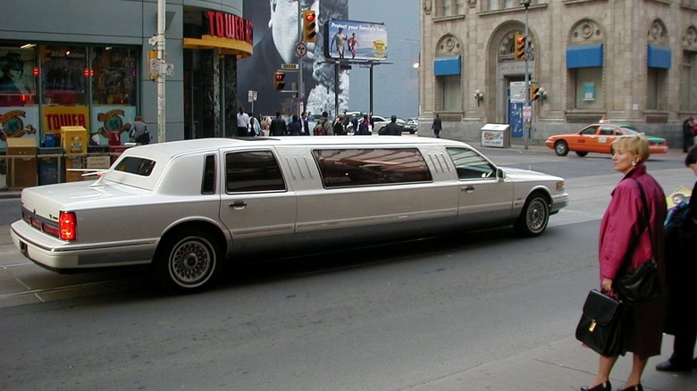 A stretch limo driving through a city street, a Tower Records in the background.