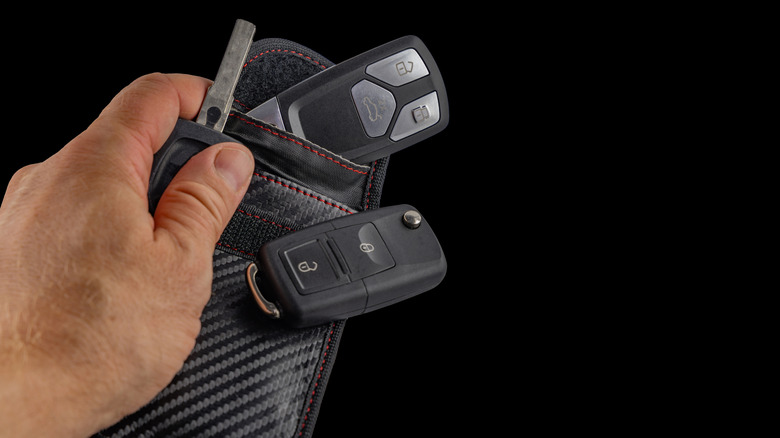 A person holding a black Faraday bag with two car keys.