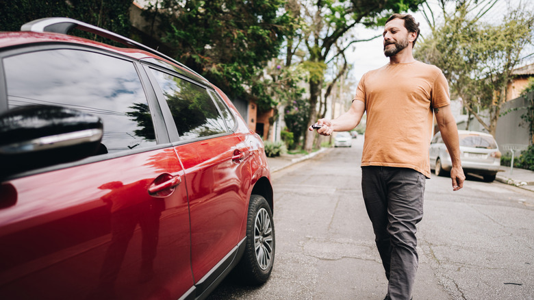 A man walking towards a red car while unlocking it.