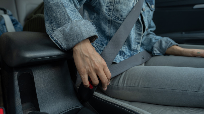A person fastening a seat belt in a car.