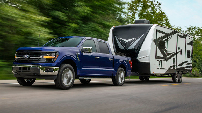A blue Ford F-150 towing a motorhome on a rural road