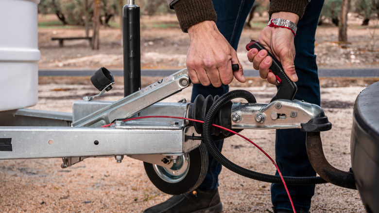 A person connecting a travel trailer to a vehicle tow bar