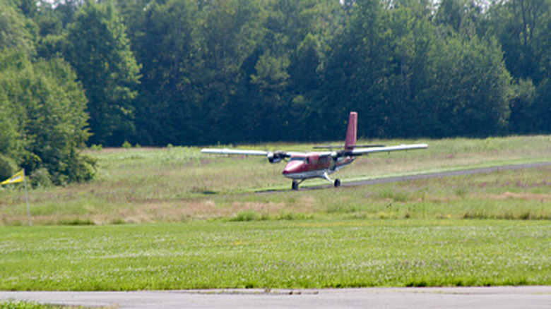 A twin-engined propeller-driven plane taking off from a short runway surrounded by trees