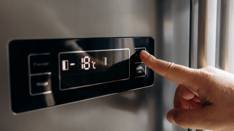 A person is using a digital temperature control panel on a refrigerator.