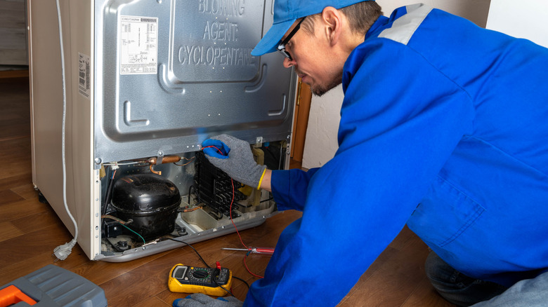 Repair work on refrigerator unit in home kitchen during afternoon hours
