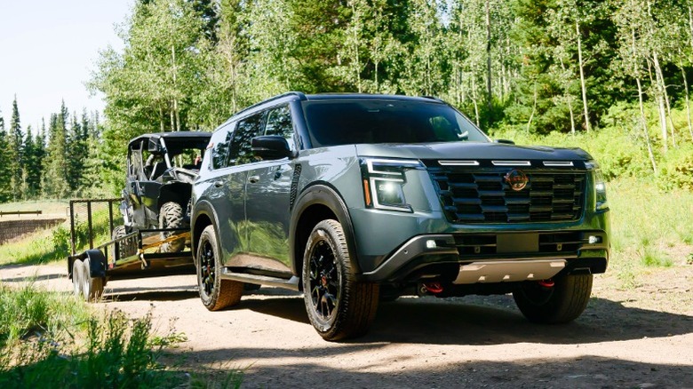Nissan Armada towing an ATV trailer on a forest trail.