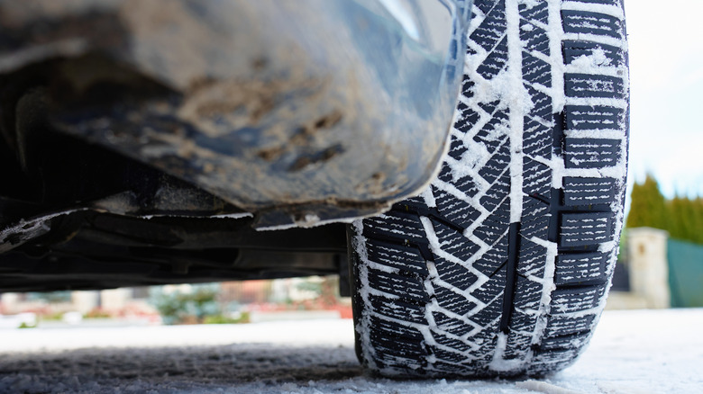 Close up of car wheel with winter tire covered in snow on icy road surface