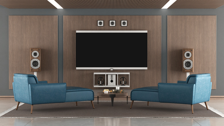 A home theater room with large TV, hi-fi loudspeakers, and two green chaise longues