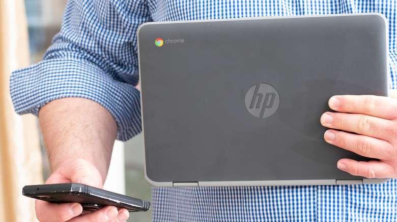 Man holding a Chromebook in one hand and a smartphone in another hand
