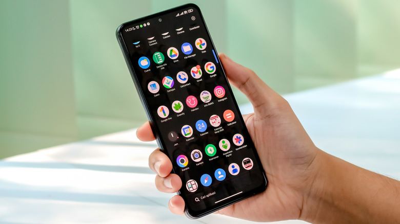 Hand holding Android phone with app drawer open onscreen