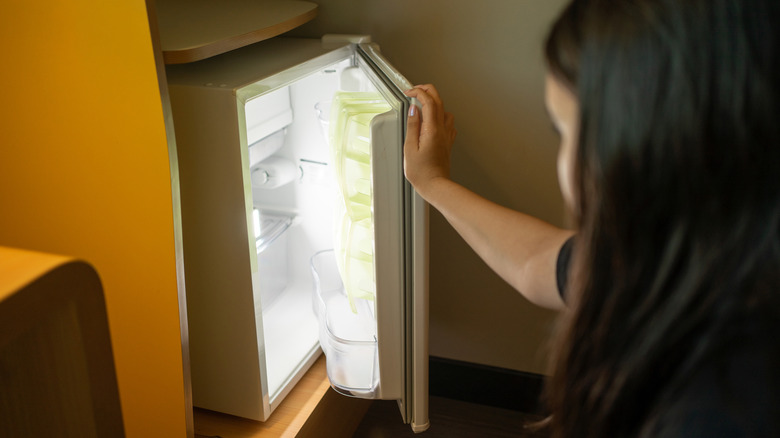 A person opens a mini fridge at floor level.