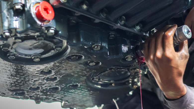 Mechanic servicing automatic transmission drain pan with pink automatic transmission fluid draining out