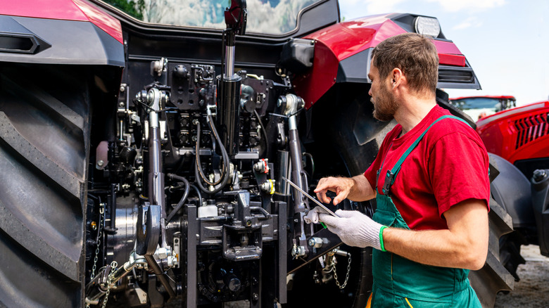 A person overlooking a tractor's mechanics.