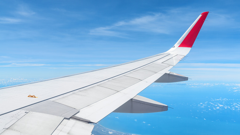A view of airplane wing with yellow hook high in the sky
