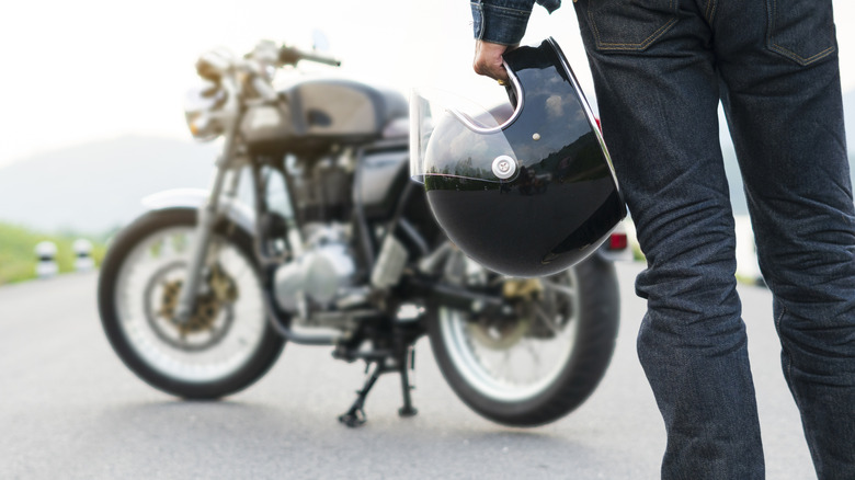 Biker riding in jean is holding a helmet and motorcycle blur background