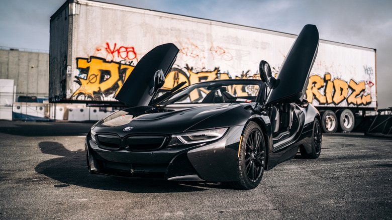 Black BMW i8 in front of grafitti-laden truck trailer, front 3/4 view