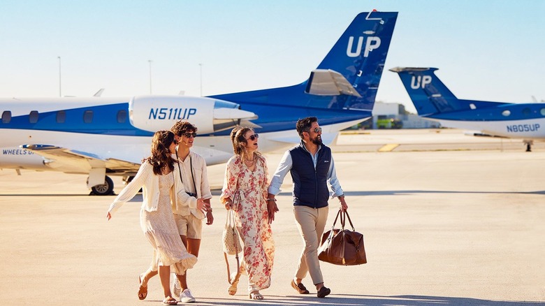 group of people walking on away from Wheels Up private jets on tarmac