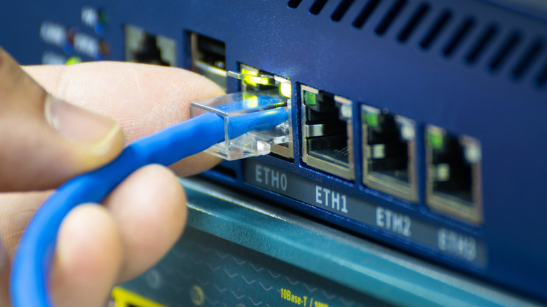 Close-up of a hand plugging a blue ethernet cable into a network switch