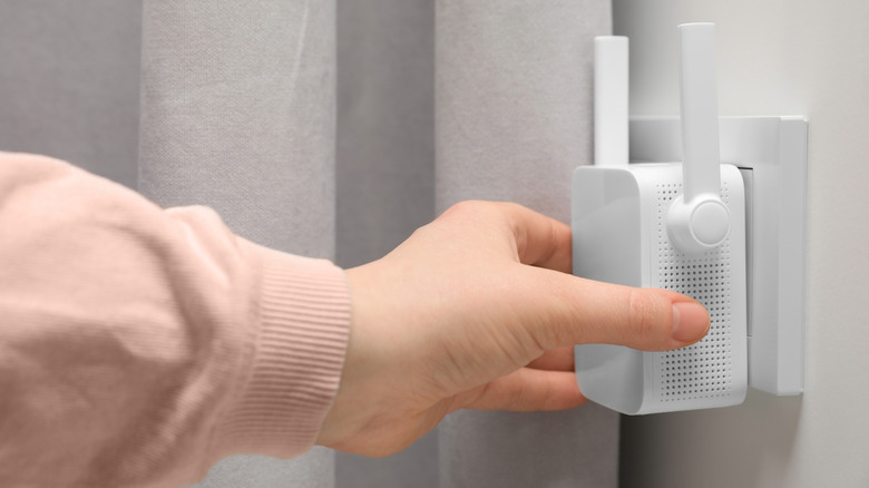 A hand plugging a Wi-Fi extender into the wall