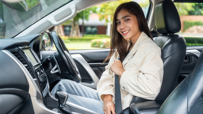 Young woman in driver's seat smiling and putting on seat belt