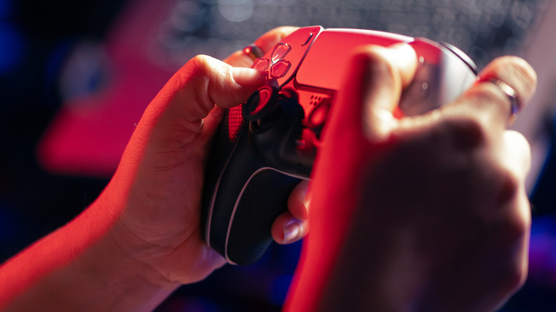A person holding a PS5 controller under red light.
