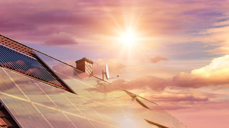 Solar panels on a house roof with the sun in the background.
